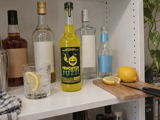0,7-l-Flasche im Regal der Hausbar, daneben ein Glas mit Eis und Zitrone
