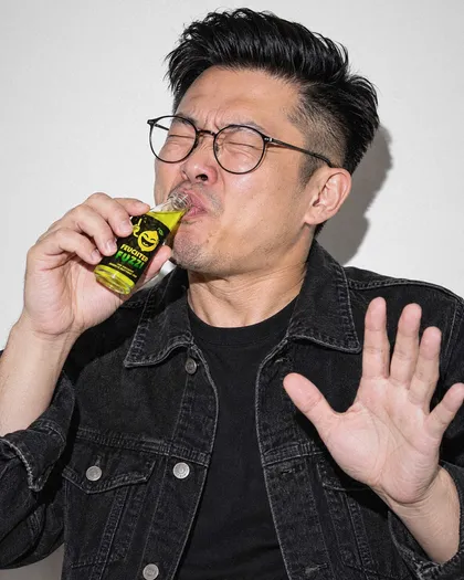 Mann mit Brille nippt am Fläschchen und hebt abwehrend die Hand