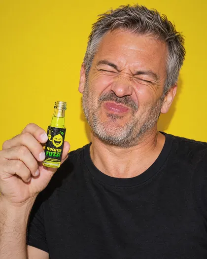 Mann mit grauem Haar hält ein offenes Feuchter-Fuzzi-Fläschchen und kneift die Augen zusammen